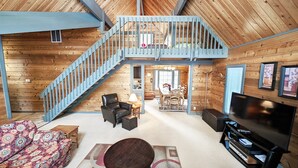 A spacious loft-style living area with a staircase, a dining table, and a television. - Lava Top 1 (Bend)