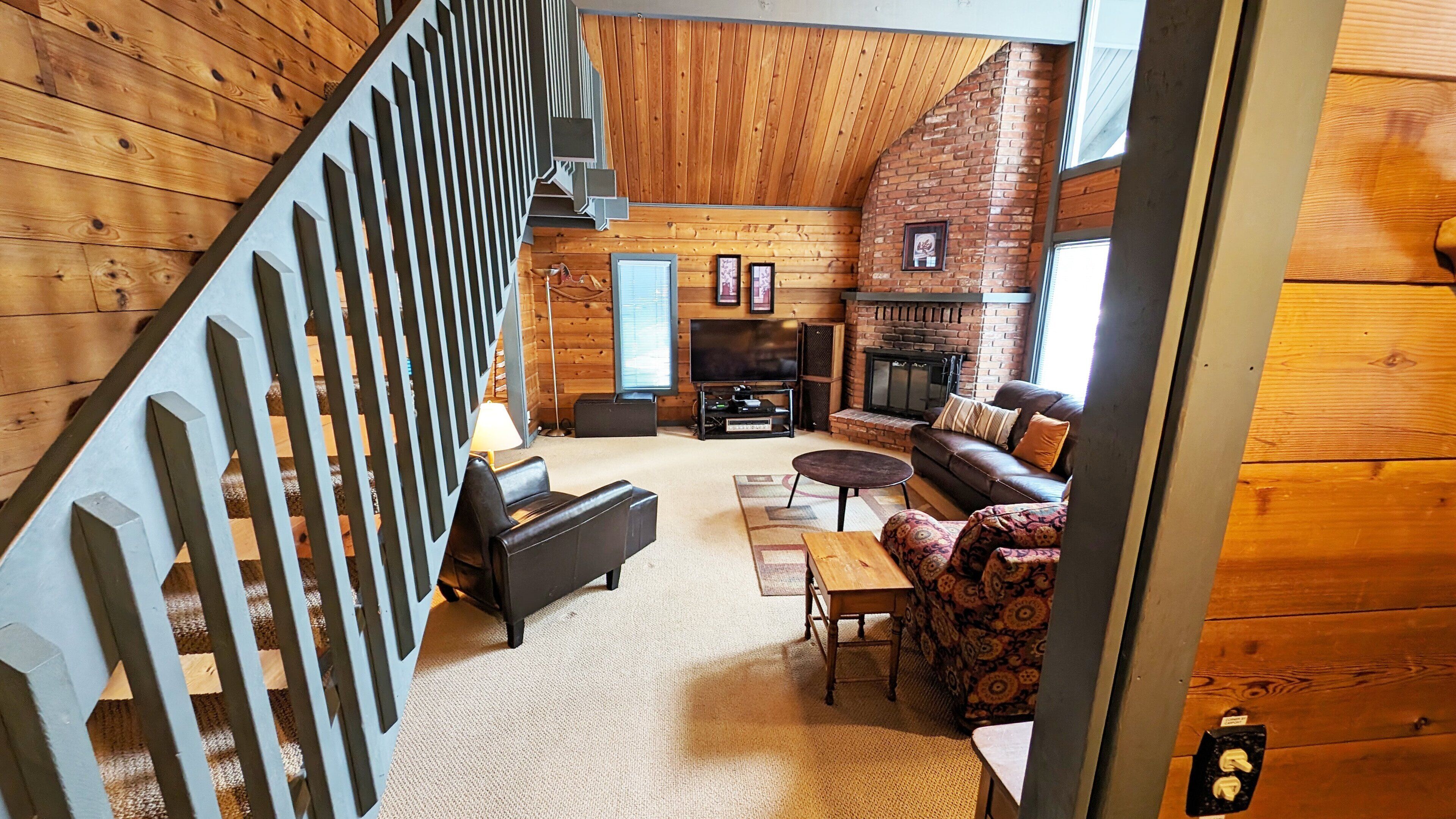 A log cabin interior with a staircase, fireplace, sofa, and a television.