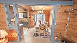 A wooden interior with a dining table, chairs, a chandelier, and a kitchen area. - Lava Top 1 (Bend)