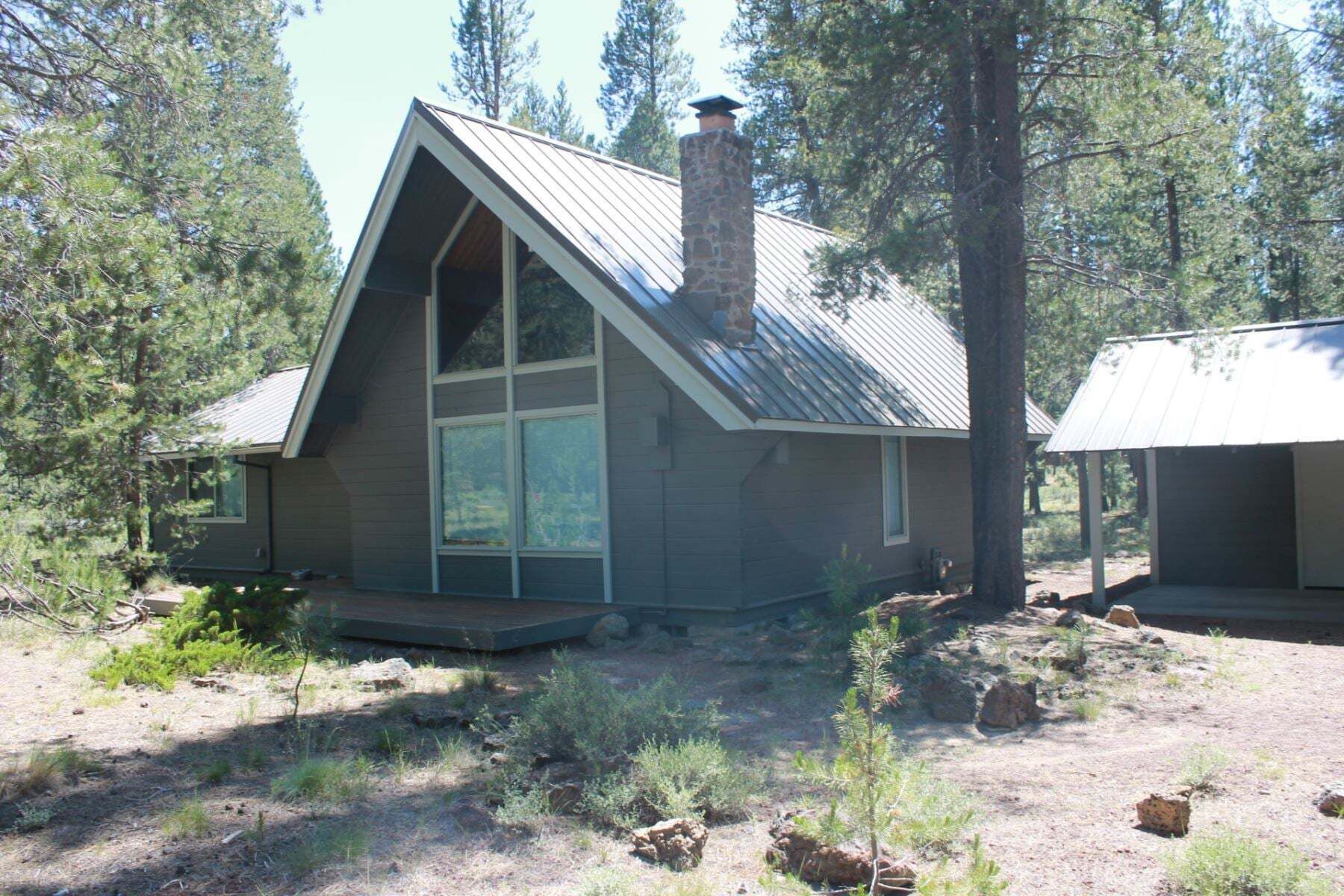 A cabin with a gabled roof, large windows, and a stone chimney.