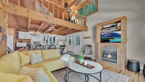 A cozy living room with a yellow sofa, a fireplace, and a dining area with a view of mountains. - Lake Wallenpaupack Lakefront Private Boat Slip (Greentown)