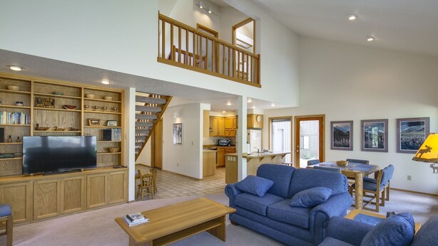 A spacious living area with a television, bookshelves, a sofa, and a staircase leading to an upper level. - Maury Mountain 36 (Bend)