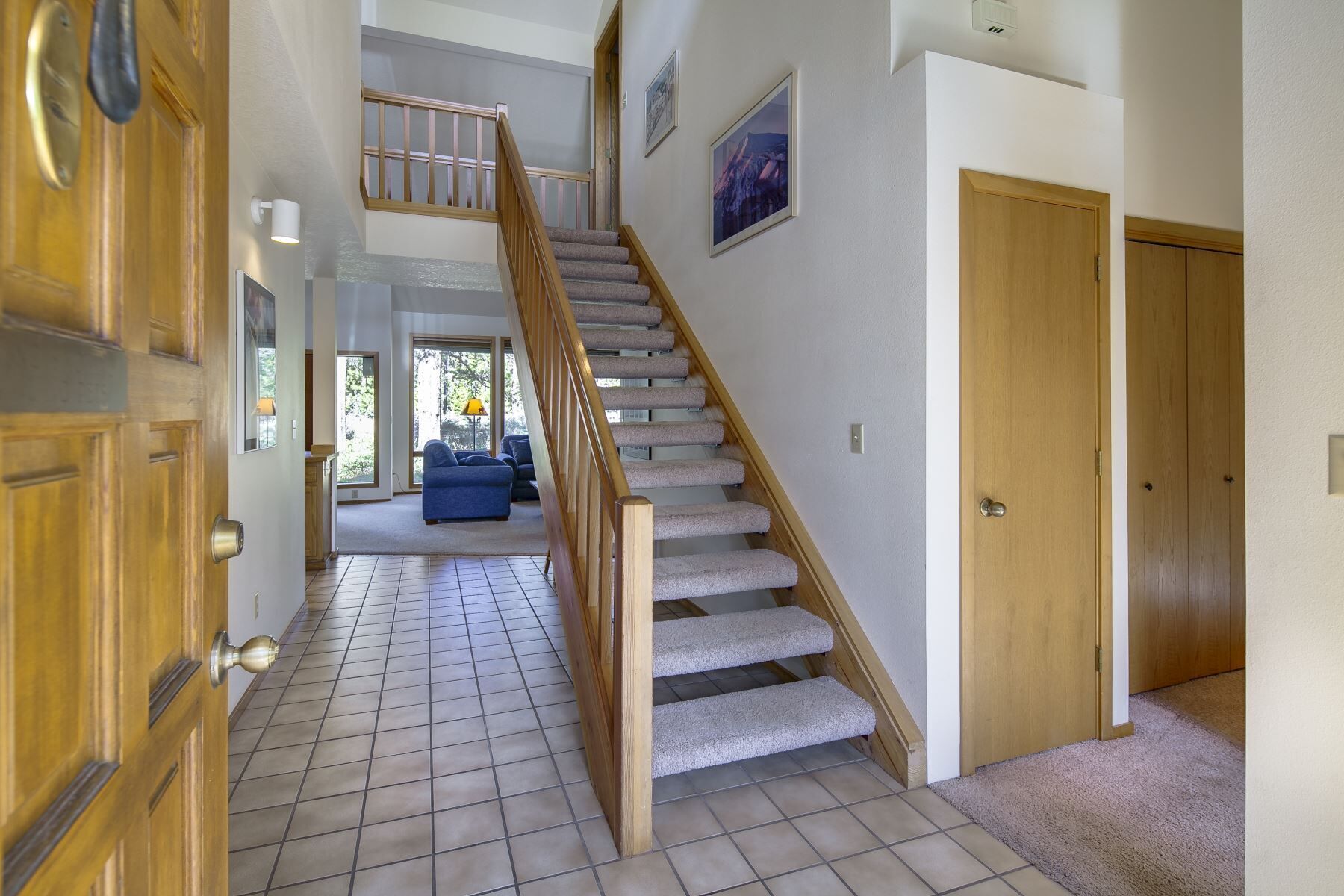 Un couloir avec un escalier en bois, un revêtement de sol carrelé et une porte dotée d’une poignée en laiton.