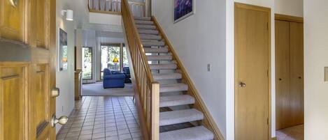 Un couloir avec un escalier en bois, un revêtement de sol carrelé et une porte dotée d’une poignée en laiton.
