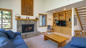 A living room with a stone fireplace, blue sofas, a wooden coffee table, and a TV. - Maury Mountain 36 (Bend)