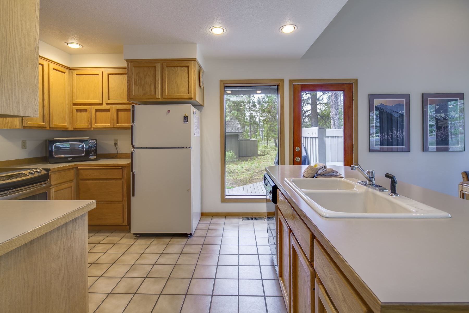 A kitchen with wooden cabinets, a refrigerator, a microwave, and a sink.