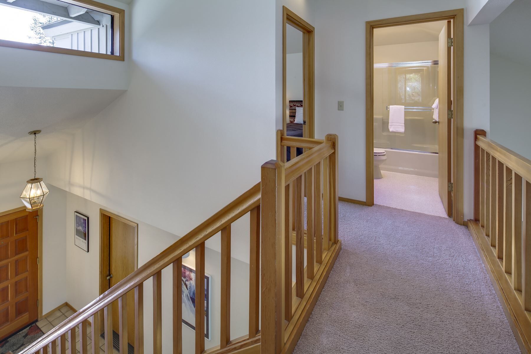 A multi-level interior with a wooden staircase, a hallway leading to a bathroom, and a visible door.