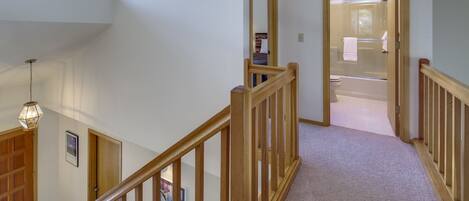 A multi-level interior with a wooden staircase, a hallway leading to a bathroom, and a visible door.