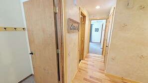 A hallway with wooden flooring, a door on the left, and a framed picture on the wall.