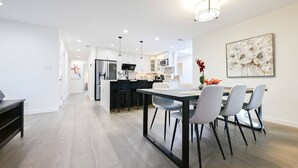 A modern kitchen with white cabinets, a central island, and a dining area with a table and chairs. - Marbella Lane - Exquisite Home 3BR (Sunnyvale)