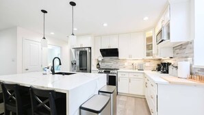 A modern kitchen with white cabinets, stainless steel appliances, and a central island with bar stools. - Marbella Lane - Exquisite Home 3BR (Sunnyvale)
