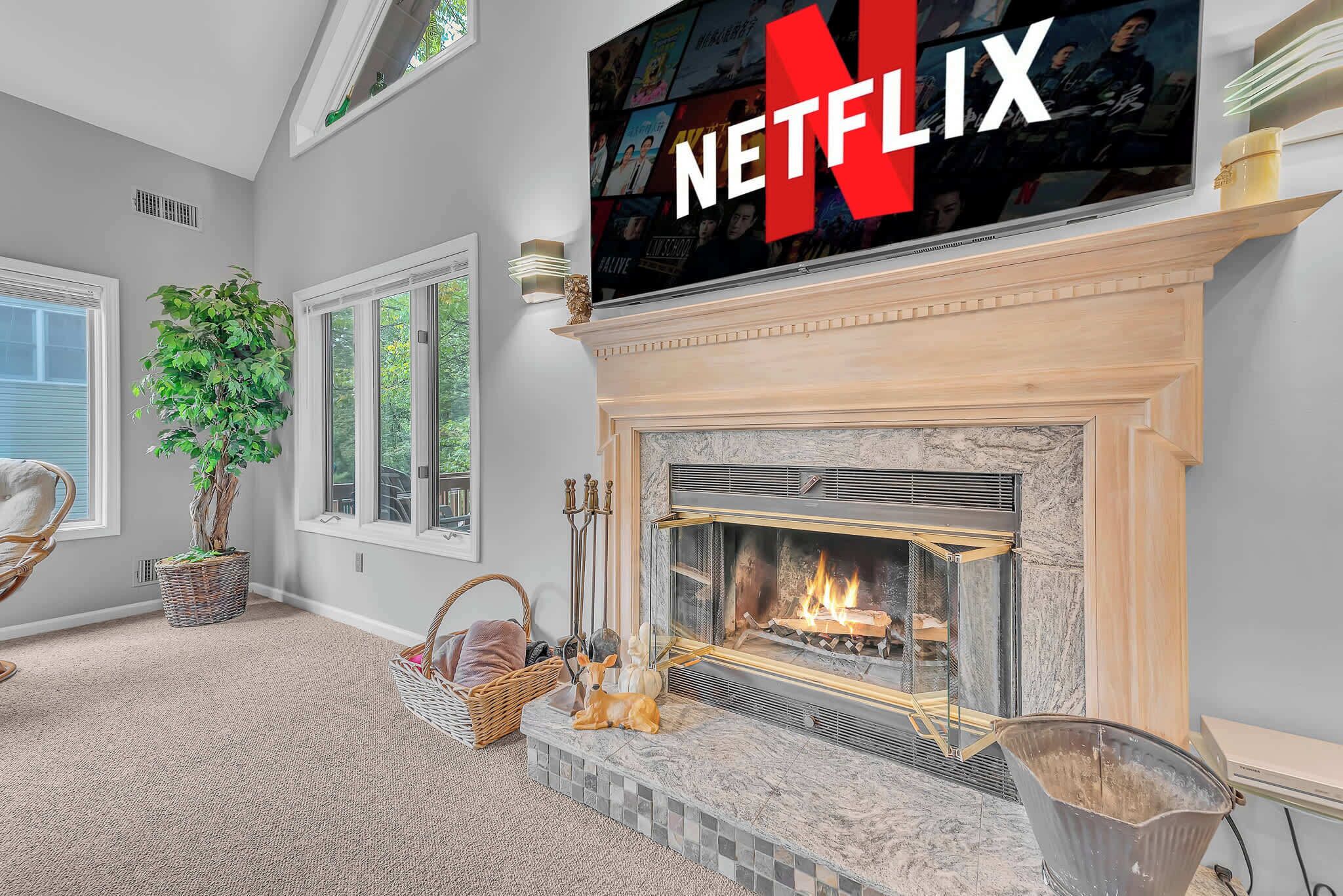 A cozy living room with a fireplace, a large TV mounted above it, and a comfortable seating area with a plant and a decorative dog statue.