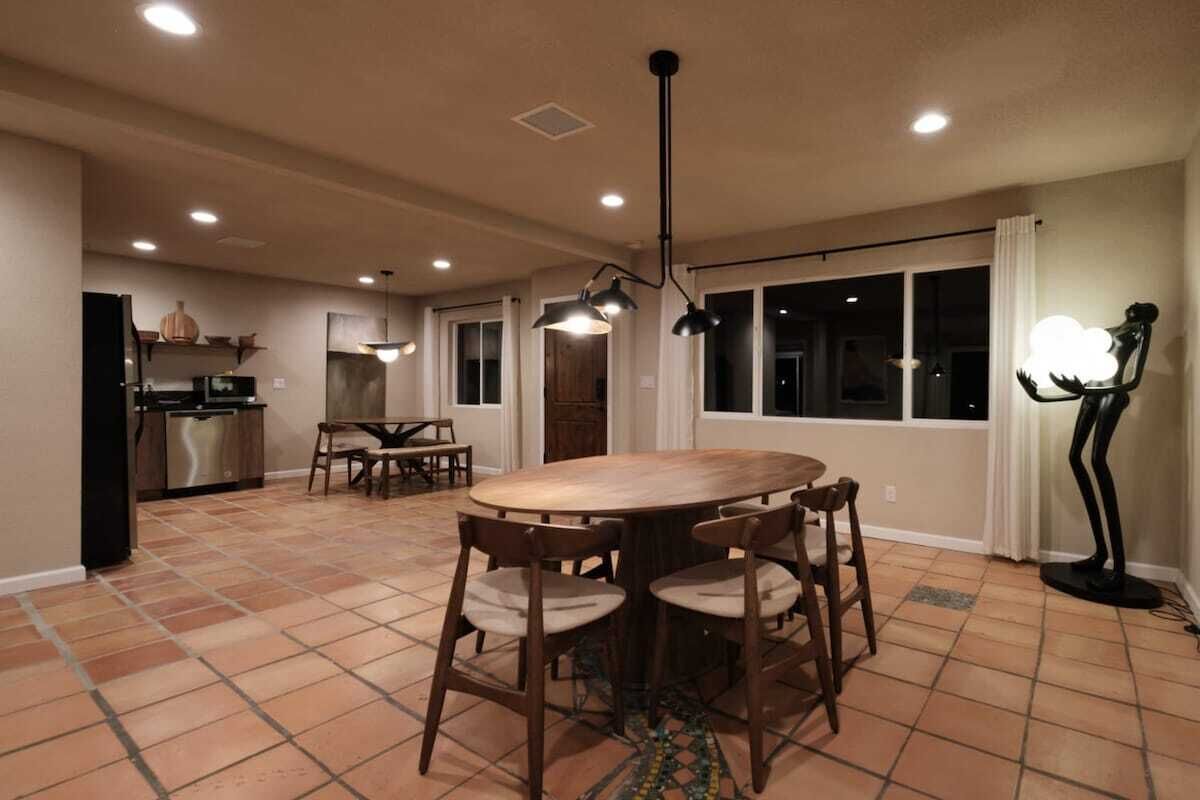 Une cuisine spacieuse avec un coin repas, comprenant une grande table ronde et des chaises, un luminaire suspendu moderne et une vue par les fenêtres.