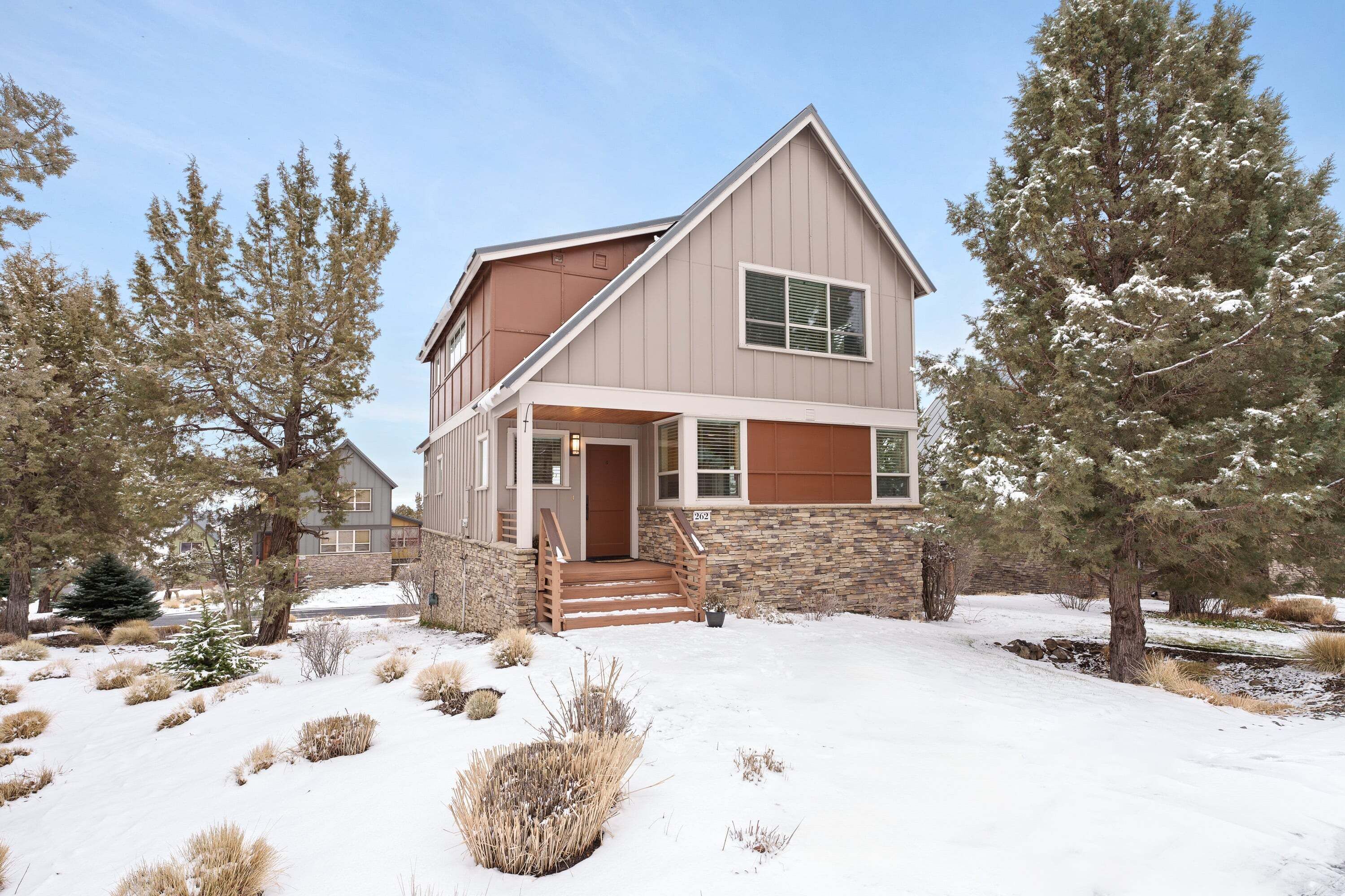 A two-story house with a stone foundation, a brown roof, and a front porch with steps.