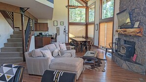 A spacious living room with a staircase, a dining area, and a stone fireplace. - Indian 3 (Bend)