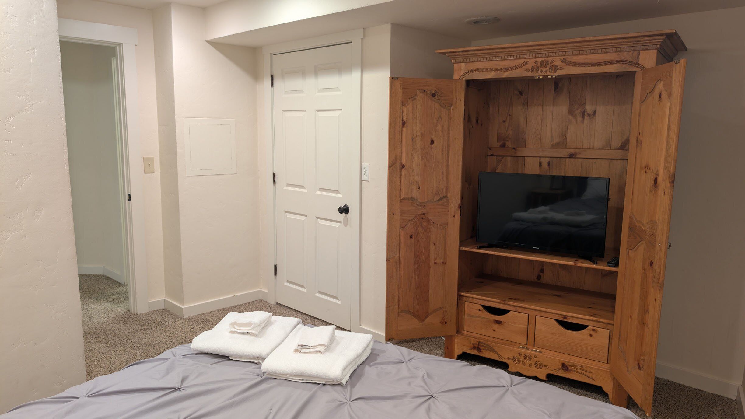 A bedroom with a bed, a wooden TV stand, and a white door.