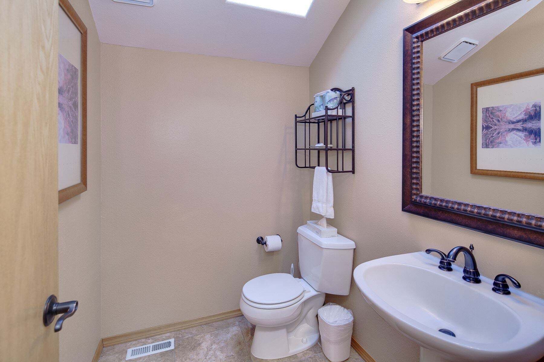 A bathroom with a toilet, sink, mirror, and towel rack.