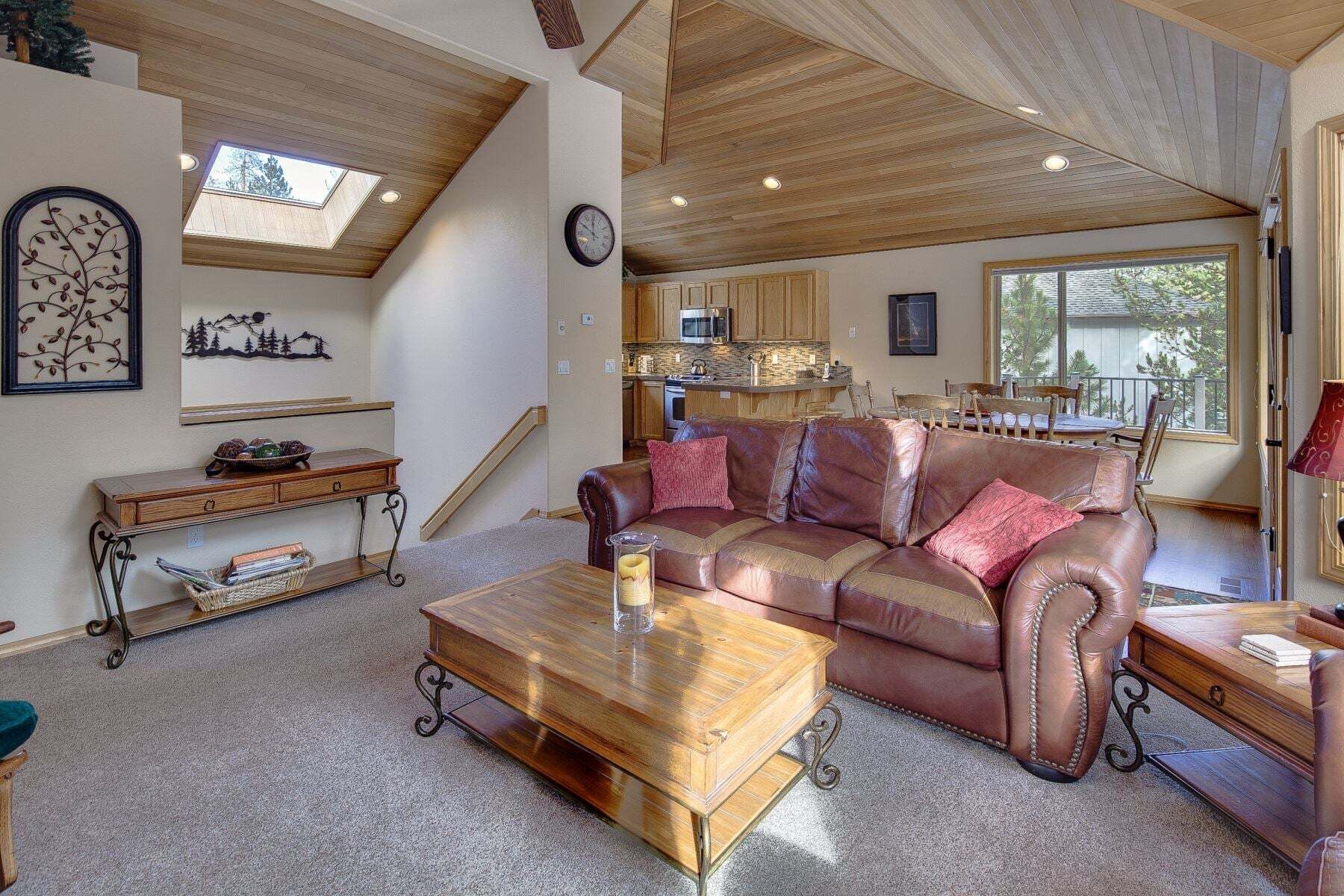 A spacious living room with a leather couch, wooden coffee table, and a kitchen in the background.