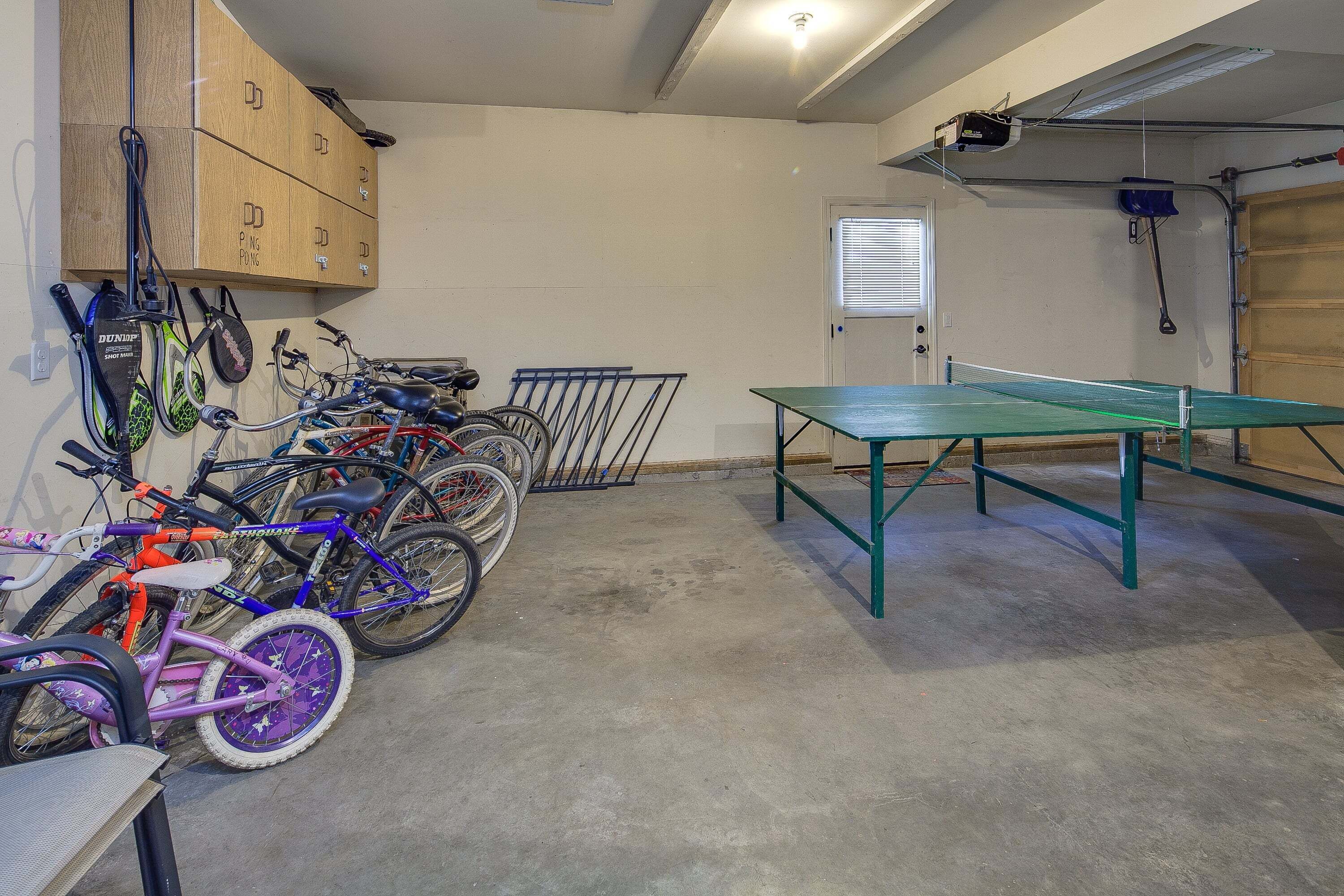 Eine Garage mit Fahrrädern, einem Tischtennisplatten und Stauraumschränken.