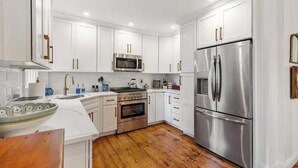 A modern kitchen with white cabinets, stainless steel appliances, and a wooden floor. - Driftwood Suite - Luxury Retreat in Newport (Newport)