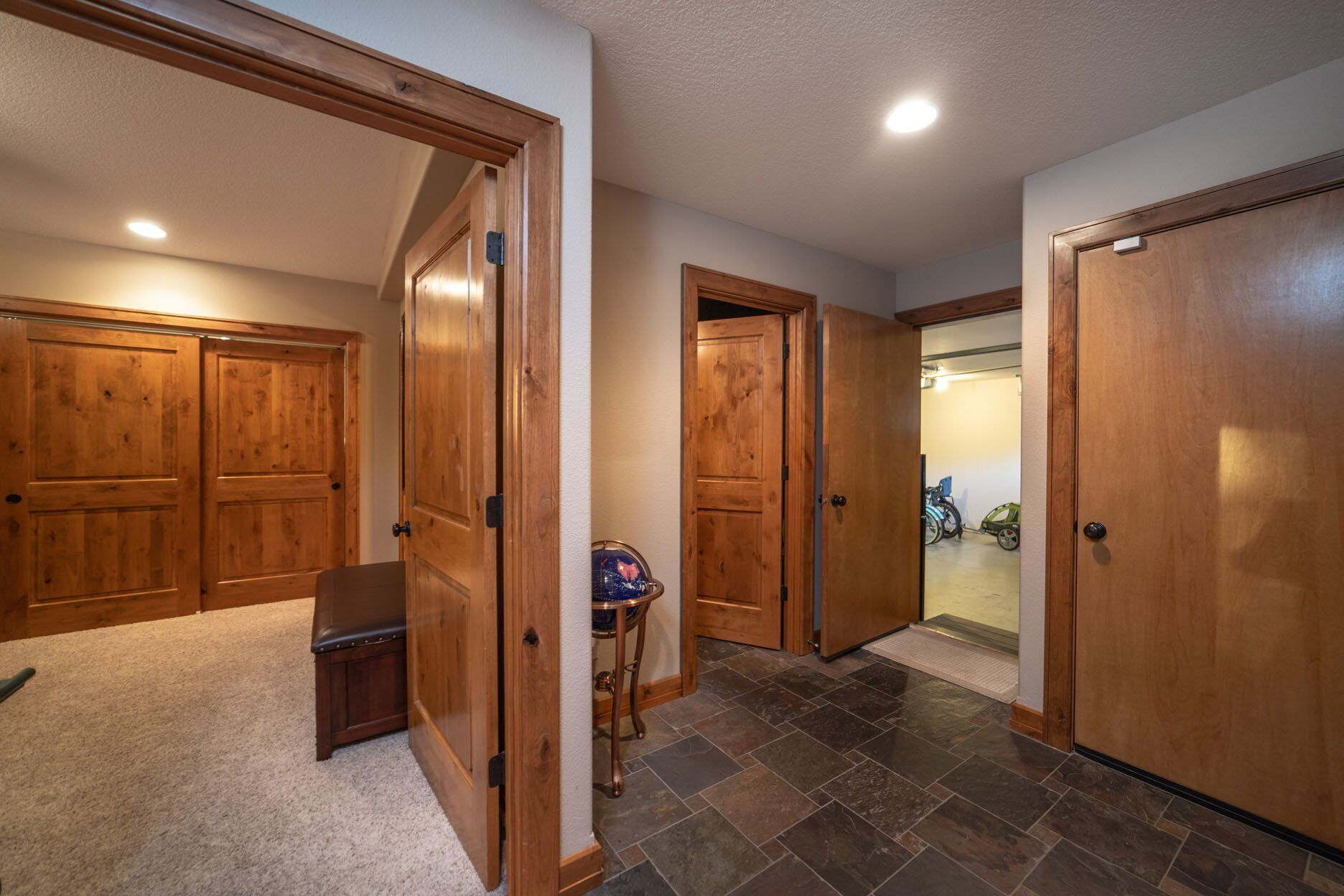 A hallway with wooden doors, a small table with a globe, and a view into a garage with a bicycle.