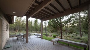 A covered deck with outdoor furniture, a view of a forested area, and a building with a window. - Yellow Pine 32 (Bend)