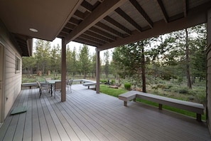 A covered deck with outdoor furniture, a view of a forested area, and a building with a window. - Yellow Pine 32 (Bend)