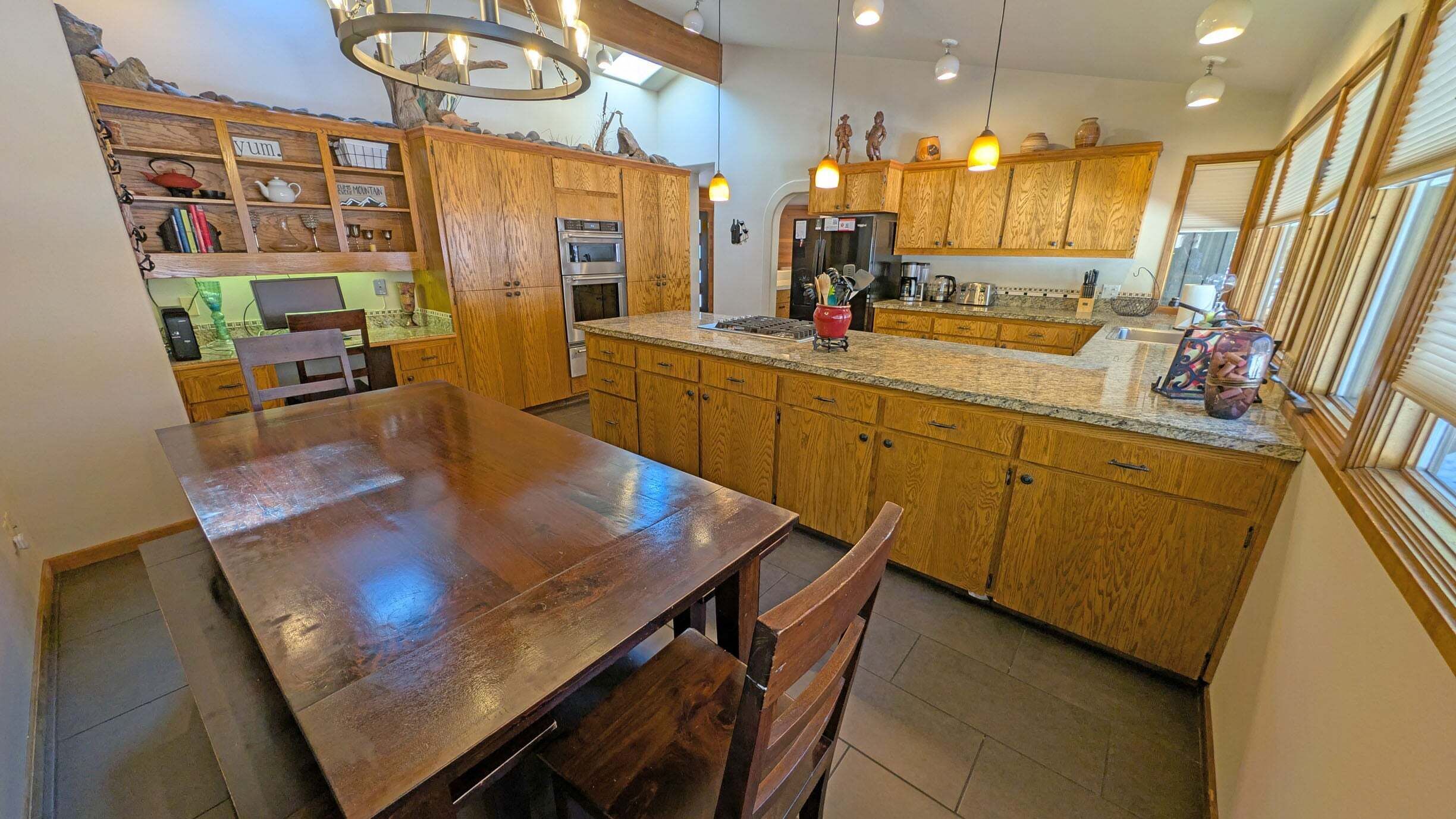 A kitchen with wooden cabinets, a granite countertop, and a dining area with a wooden table and chairs.