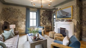 A living room with a fireplace, a sofa, a coffee table, and a blue armchair. - The Whale Suite Historic Coastal Luxury Newport (Newport)