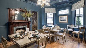 A dining room with a wooden table set for four, surrounded by wooden chairs. A fireplace with a mirror above it and a chandelier hanging from the ceiling are visible. - The Whale Suite Historic Coastal Luxury Newport (Newport)