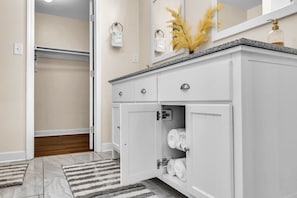 A bathroom with white cabinetry, a granite countertop, and a mirror with a golden plant decoration.