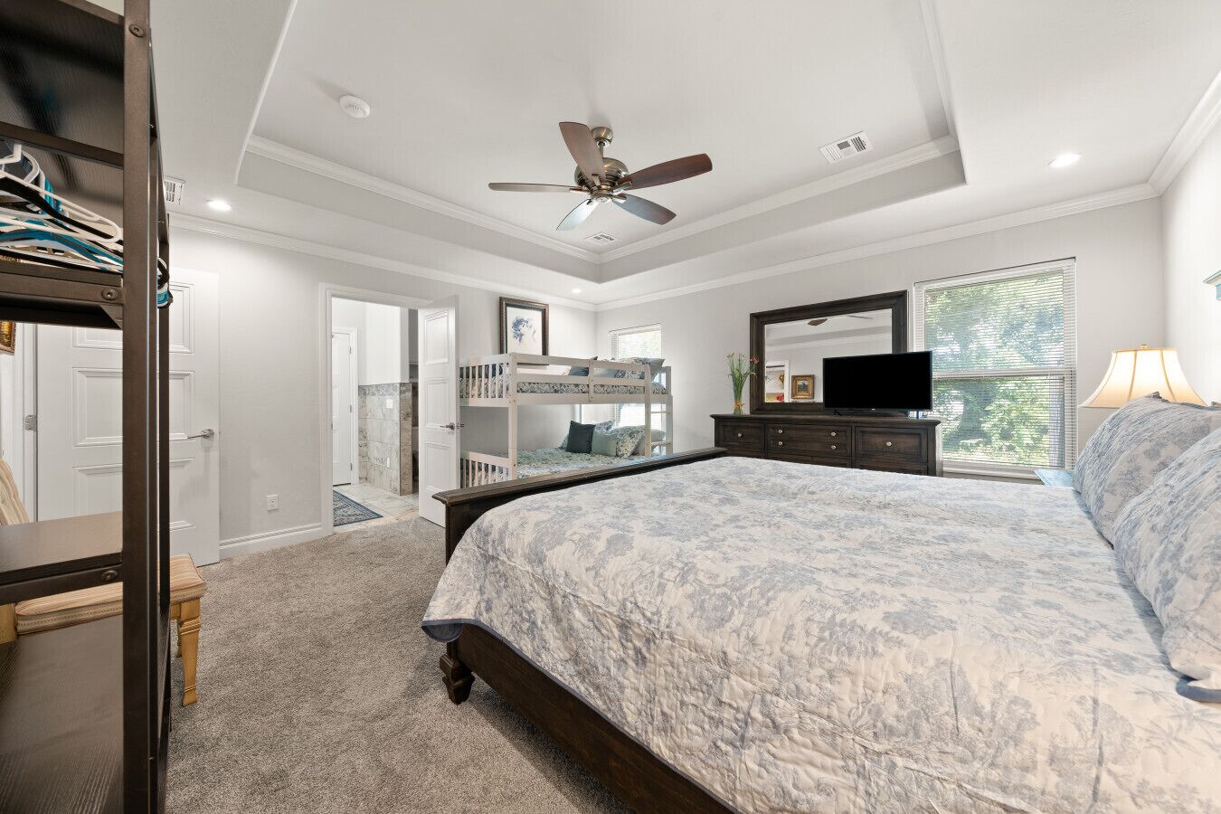 A bedroom with a large bed, a dresser, a TV, and a ceiling fan.