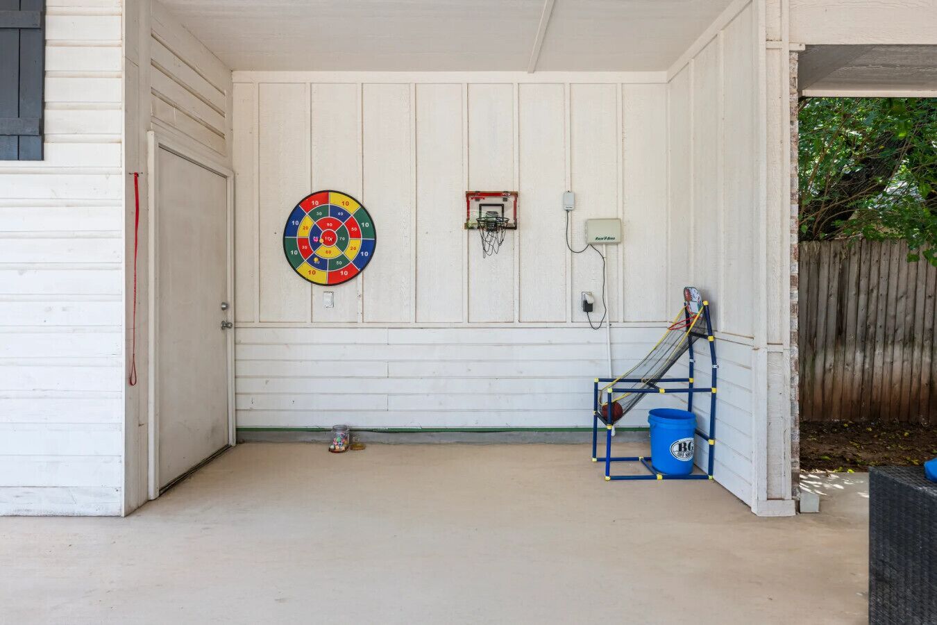 Un espacio al aire libre techado con dardos, una canasta de baloncesto y un cubo azul.