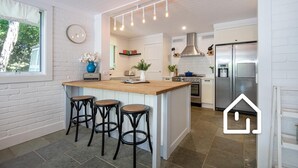 Una cocina moderna con una isla central, taburetes de bar, horno empotrado y refrigerador de acero inoxidable.