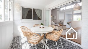 Un comedor con una mesa redonda y sillas de mimbre, una pared de ladrillo blanco y un suelo con diseño.