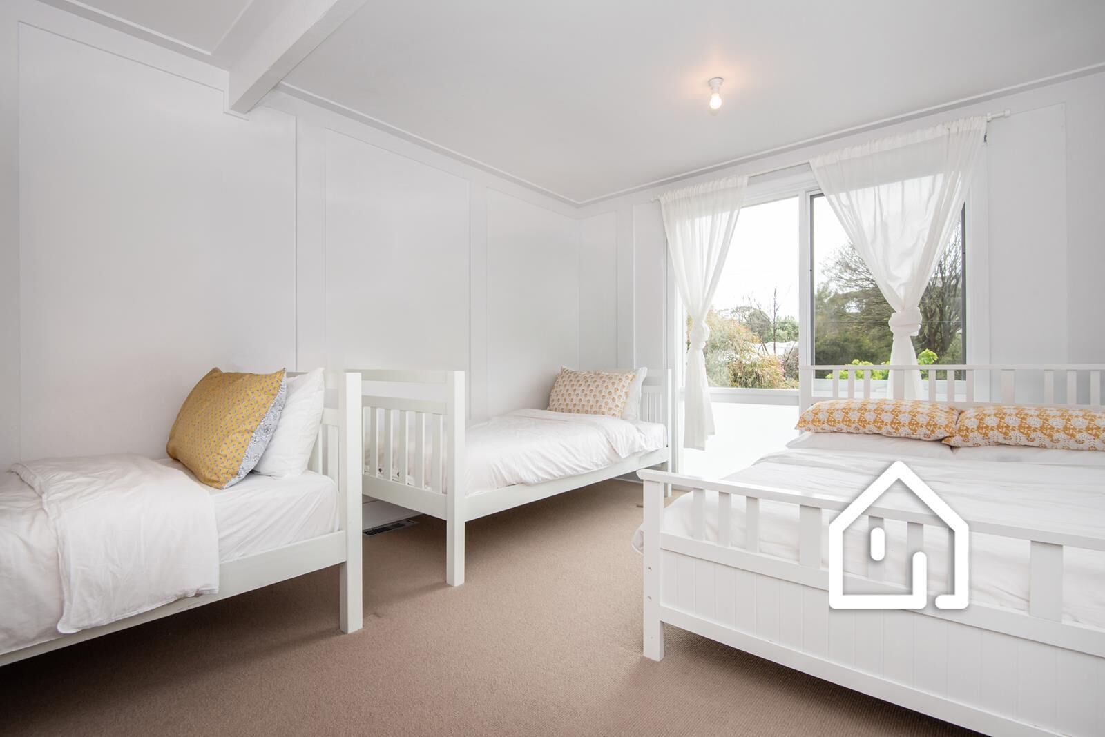Een kamer met drie witte bedden, een raam met dunne gordijnen en een witte plafondlamp.
