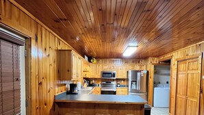 Ein Holzhütten-Interieur mit Küchenzeile, einschließlich einer Kochinsel, Barhocker und einem Kühlschrank.