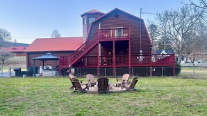Ein rustikales Holzhaus mit roter Fassade, einem Balkon und einem Feuerstellenbereich mit Adirondack-Stühlen.