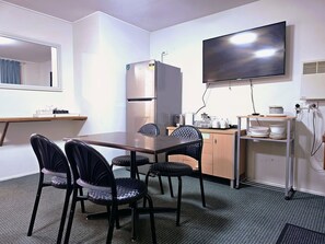 A small, well-lit room with a dining table, four chairs, a refrigerator, a television mounted on the wall, and a kitchenette area with a sink and countertop. - Room 01 : Cozy Studio 4 Guests Central Walk / In The Heart Of Jindabyne (Jindabyne)