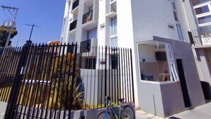 Un edificio moderno de varios pisos con balcones, una bicicleta estacionada adelante y un cielo azul despejado.