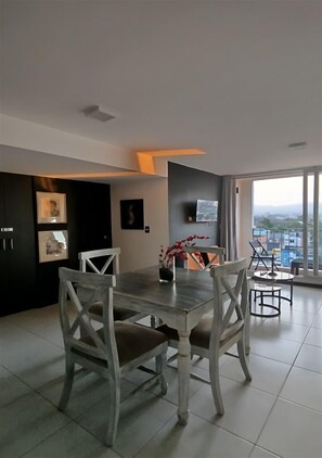 Ein moderner Essbereich mit großem Tisch und Stühlen, einem an der Wand befestigten Flachbildfernseher und Blick auf die Stadt durch große Fenster.