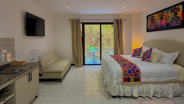 Ein modernes Hotelzimmer mit Bett, Sofa, Fernseher und einem Balkon mit Blick ins Grüne.