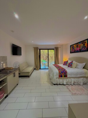Quarto de hotel moderno com cama, sofá, televisão e varanda com vista para o verde.