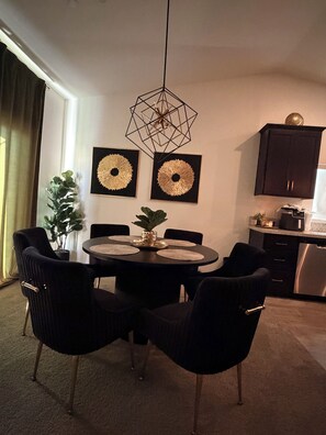 A dining area with a round table, black chairs, and two wall-mounted gold decorative pieces. - GOLDEN RAVEN House (Indio)