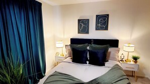 A bedroom with a bed, two bedside tables with lamps, a ceiling fan, and two wall art pieces. - GOLDEN RAVEN House (Indio)