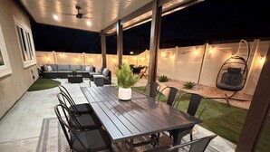 An outdoor patio with a wooden table and chairs, a sofa, and a hanging chair. - GOLDEN RAVEN House (Indio)