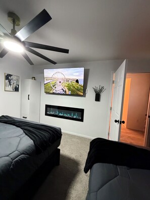 Ein Schlafzimmer mit einem Bett, einem an der Wand montierten Fernseher, einem Deckenventilator und einer Tür zu einem anderen Raum.