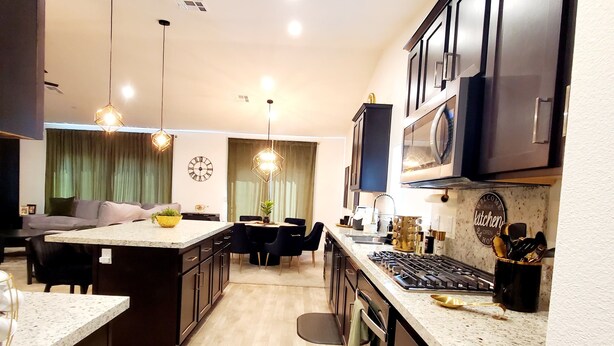 A modern kitchen with dark cabinetry, a central island, and pendant lighting. - GOLDEN RAVEN House (Indio)