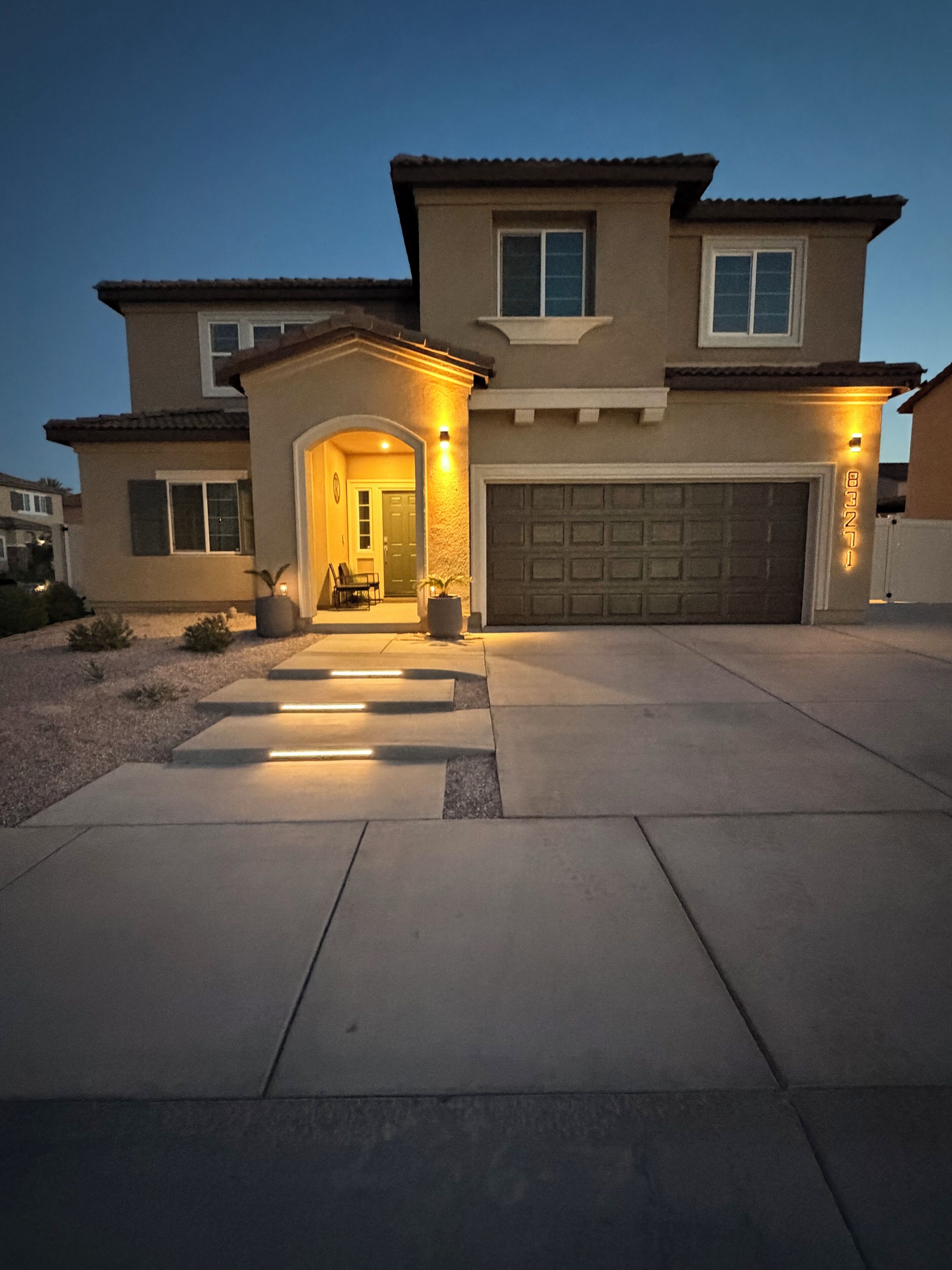 A two-story house with a garage, a covered entryway, and a well-lit driveway.
