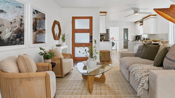 Un salon moderne avec une table basse en verre, des canapés de couleur beige et une cuisine en arrière-plan.